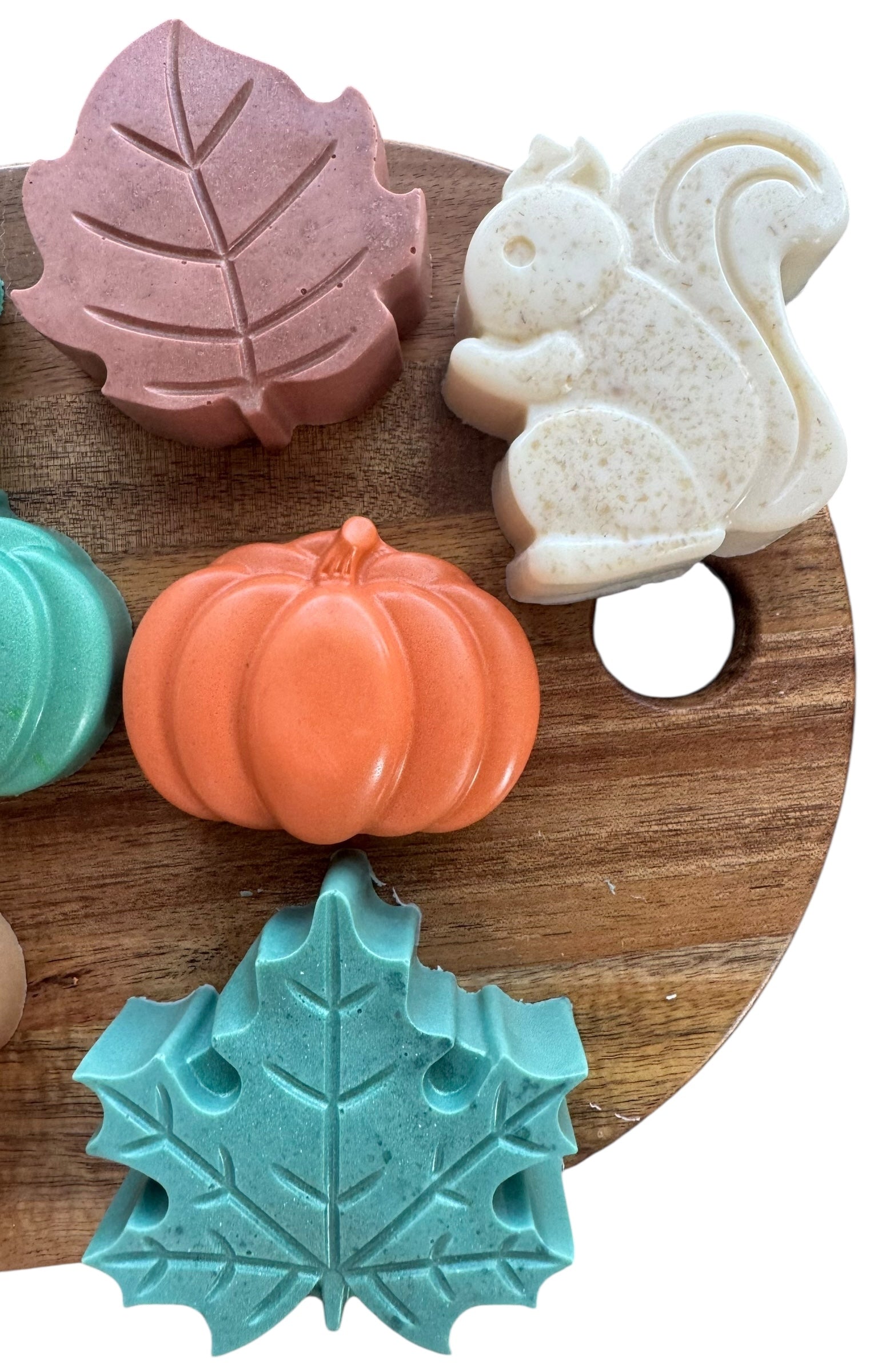 Set of colorful soap bars shaped like a leaf, pumpkin, and squirrel on a wooden board.