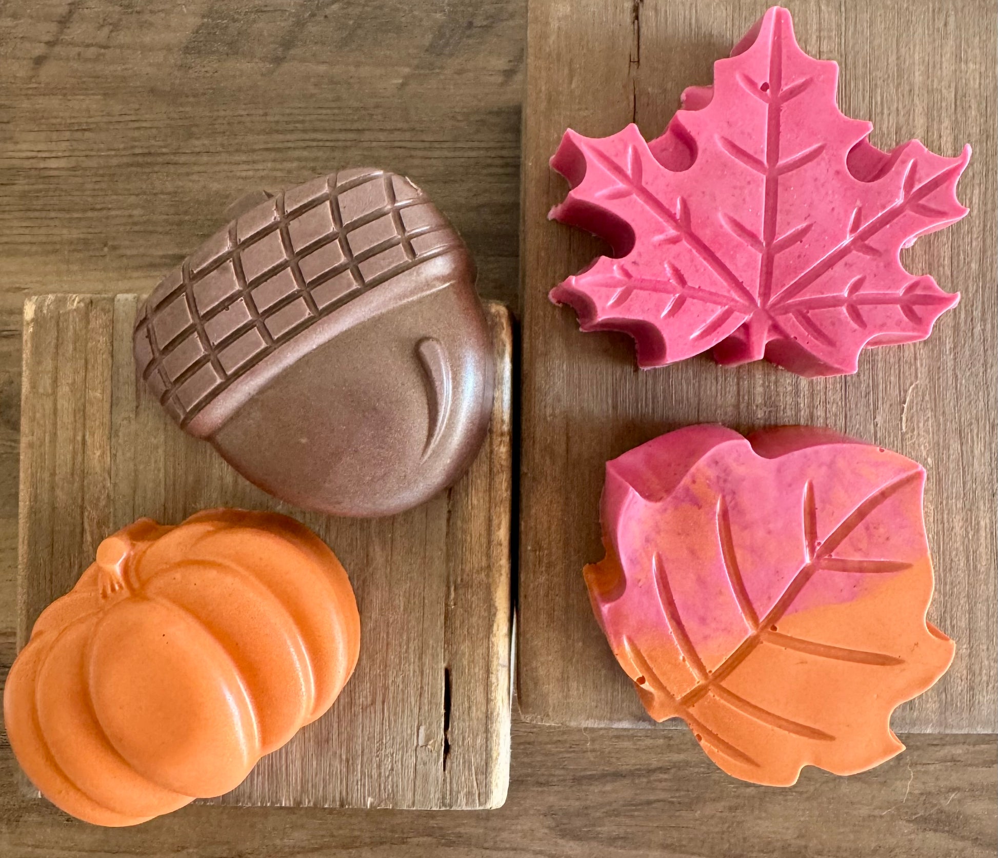 Three soap molds shaped like an acorn, pumpkin, and leaf on a wooden surface.
