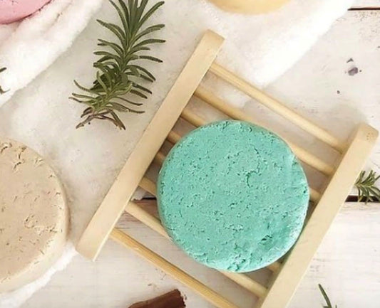 Two bath bombs, one green and one beige, on a wooden stand with rosemary sprigs.
