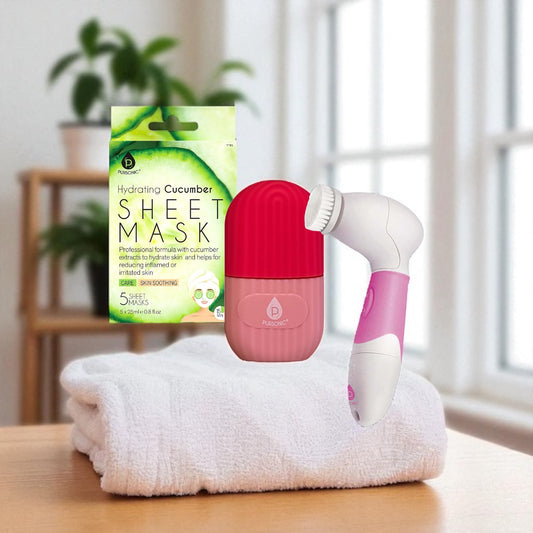 Pink and white facial cleansing device on a towel with a cucumber sheet mask in the background.