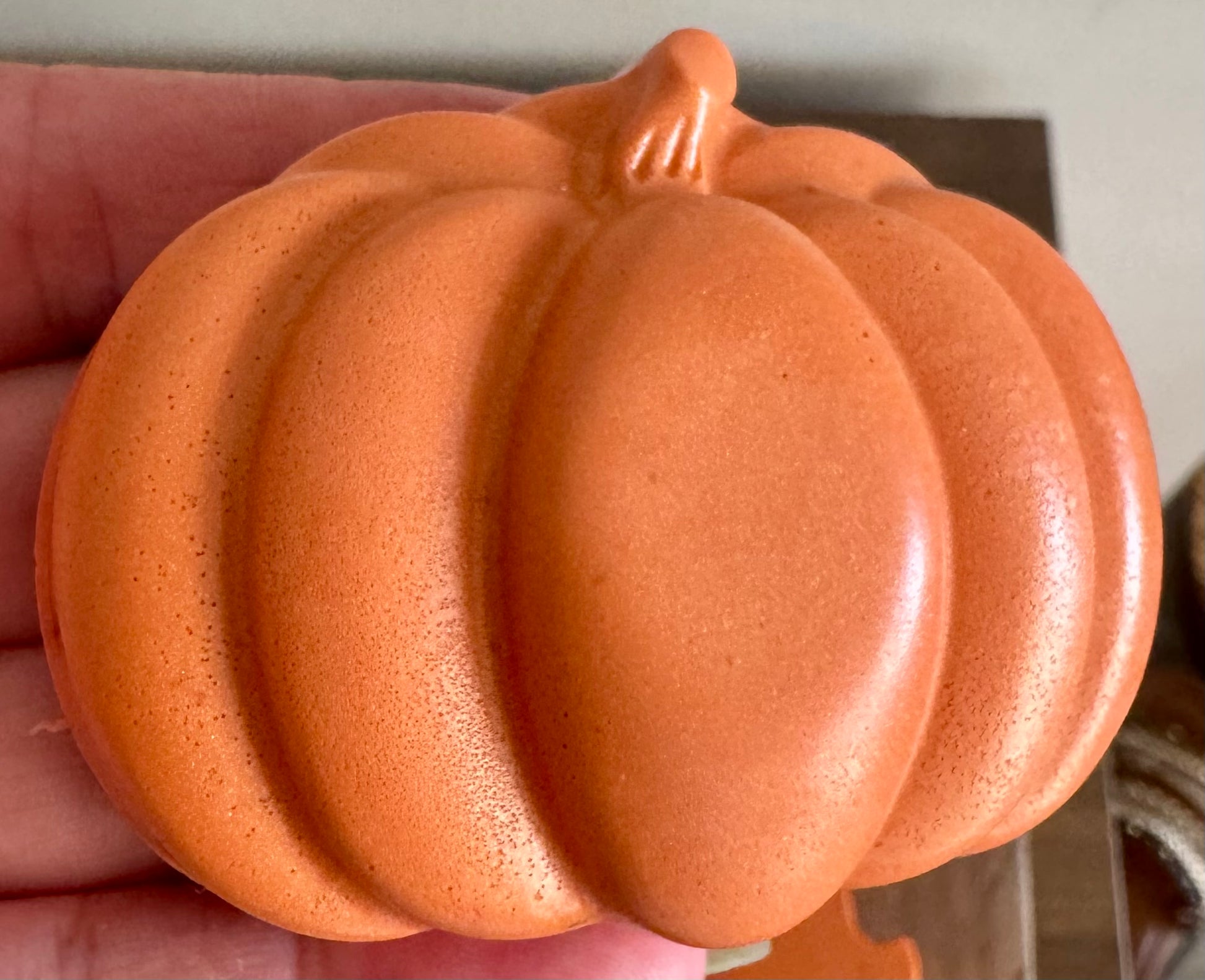Orange ceramic pumpkin held in a hand against a neutral background