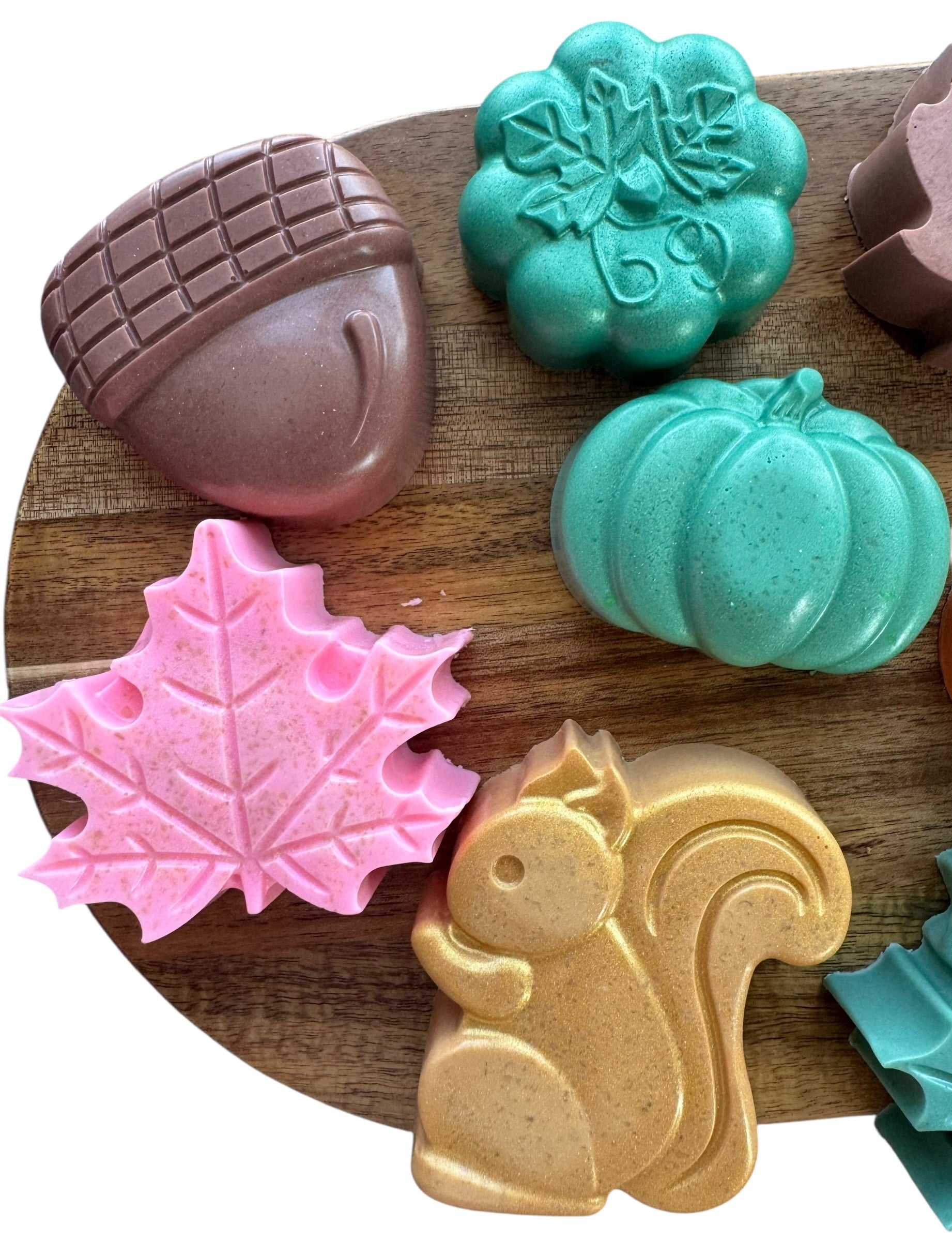 Set of colorful soap molds shaped like an acorn, leaf, pumpkin, and squirrel on a wooden surface.