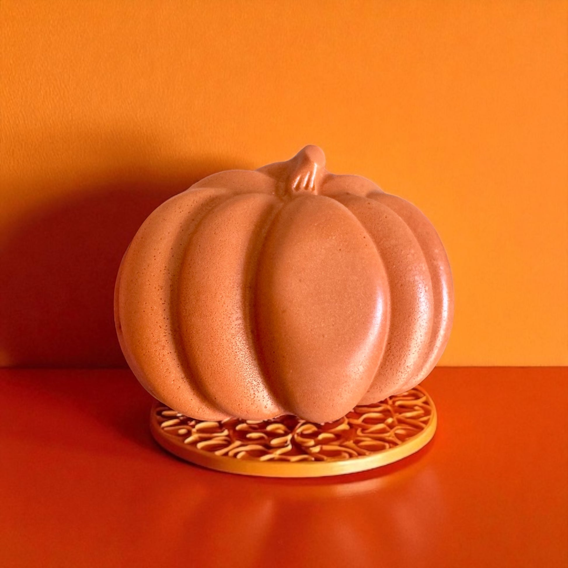 Ceramic pumpkin on a decorative stand against an orange background