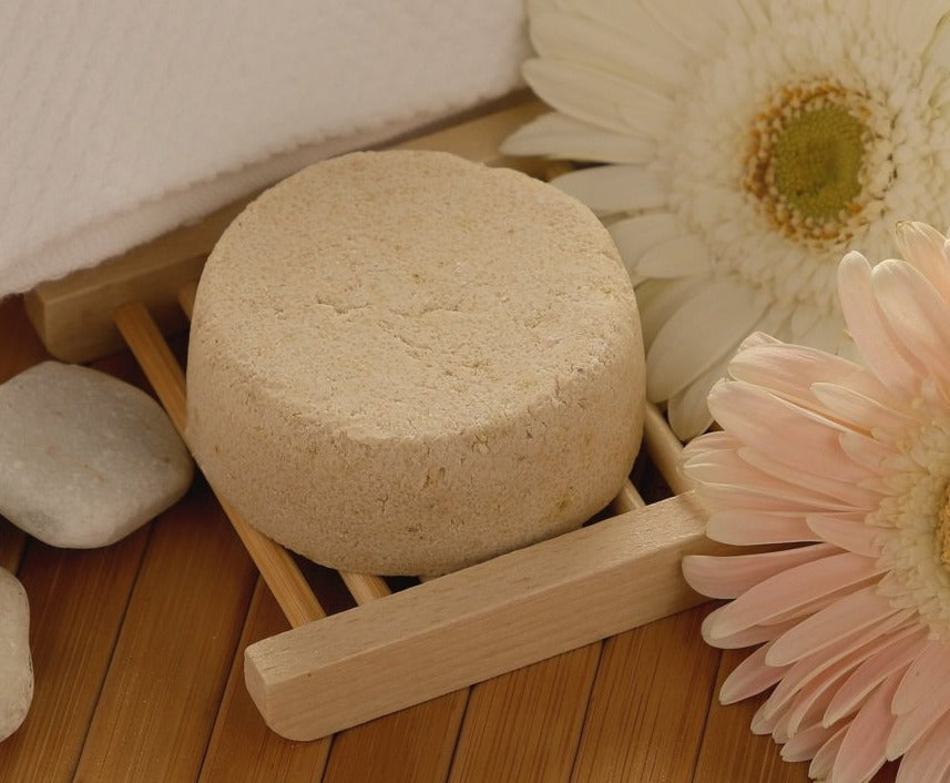 Round beige soap bar on a wooden stand with flowers and stones on a wooden surface
