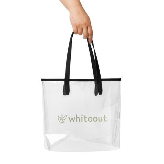 Clear tote bag with black handles held by a hand on a white background, featuring the brand 'whiteout'.