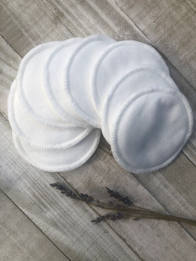 Stack of white reusable menstrual pads on a wooden surface with lavender flowers.