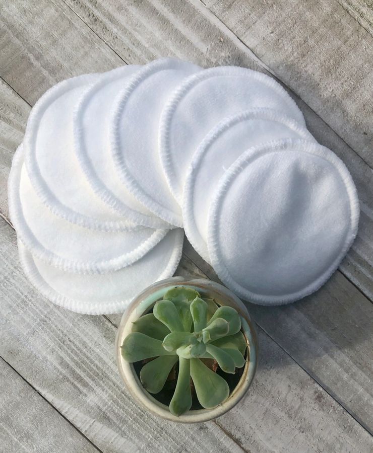 Stack of white reusable makeup pads on a wooden surface with a small potted plant.