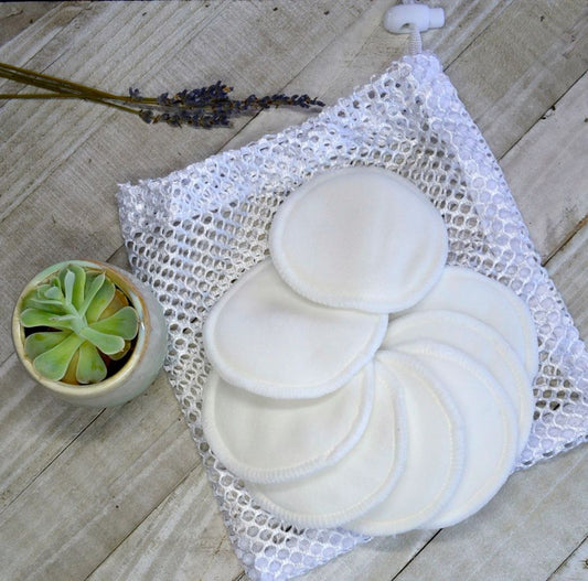 Set of reusable makeup pads in a mesh bag on a wooden surface with a small plant.