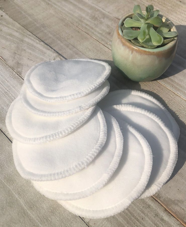 Set of white reusable makeup pads on a wooden surface with a small plant in the background.