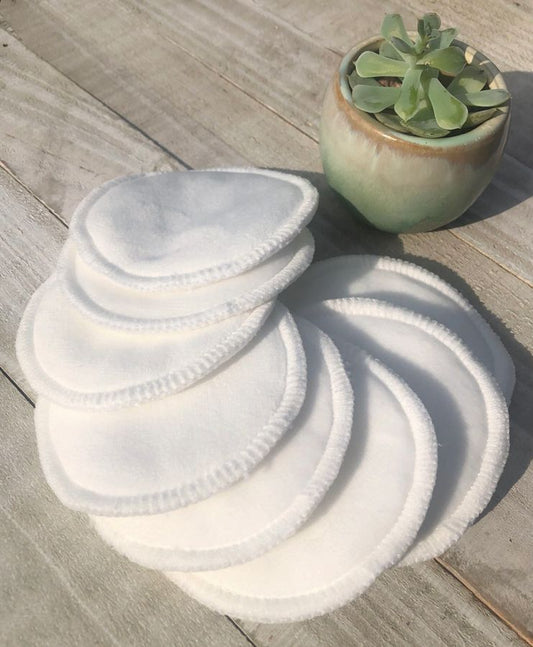 Set of white reusable makeup pads on a wooden surface with a small plant in the background.